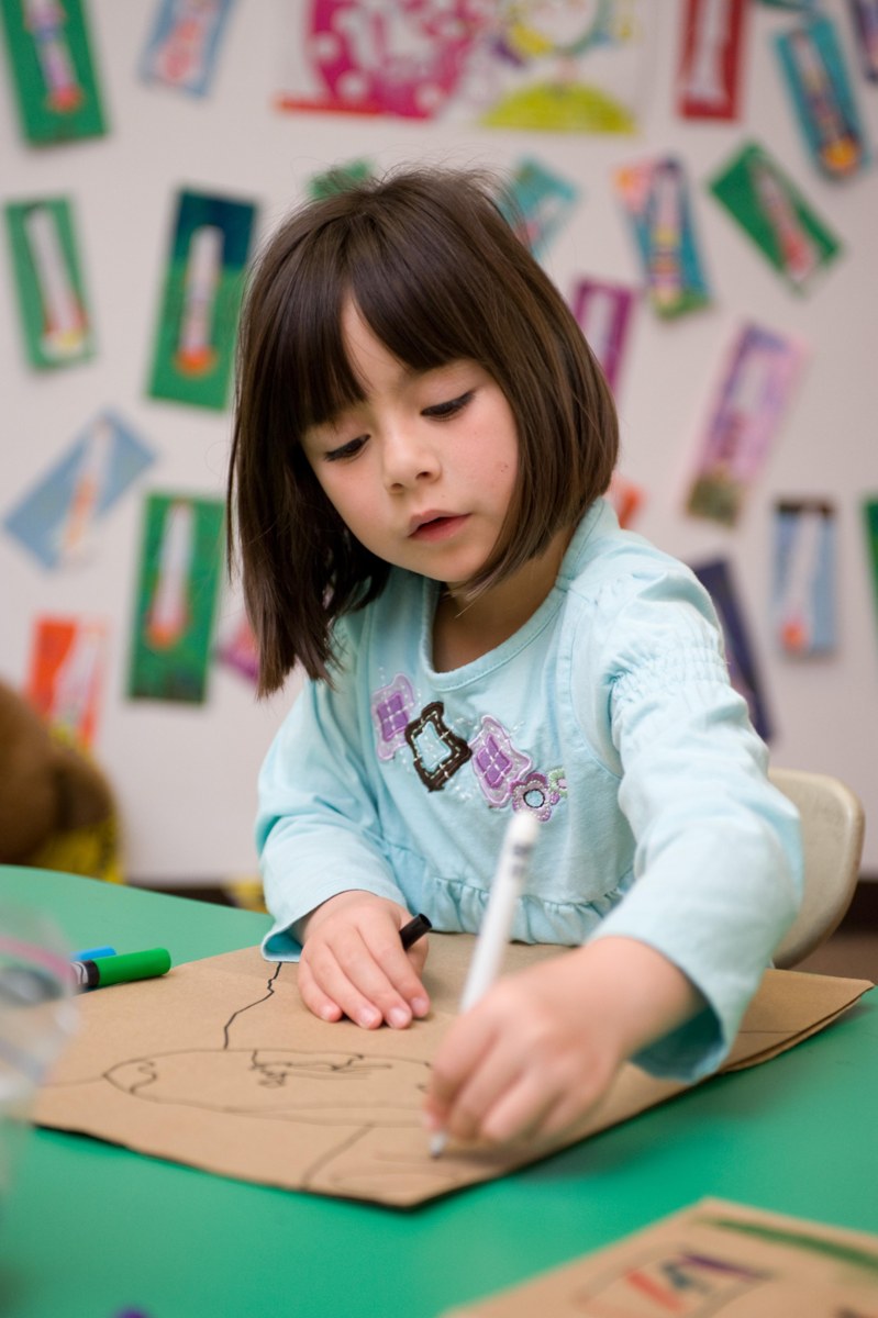 A child carefully drawing on a paper bag during a classroom art project